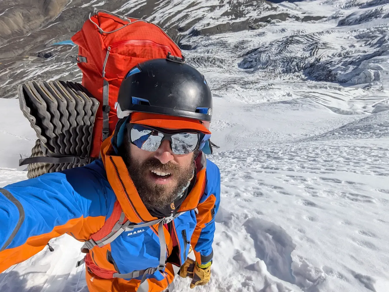 Alberto Viseras, founder of Altura Expeditions, high on a snow slope in mountaineering kit with a glacier below