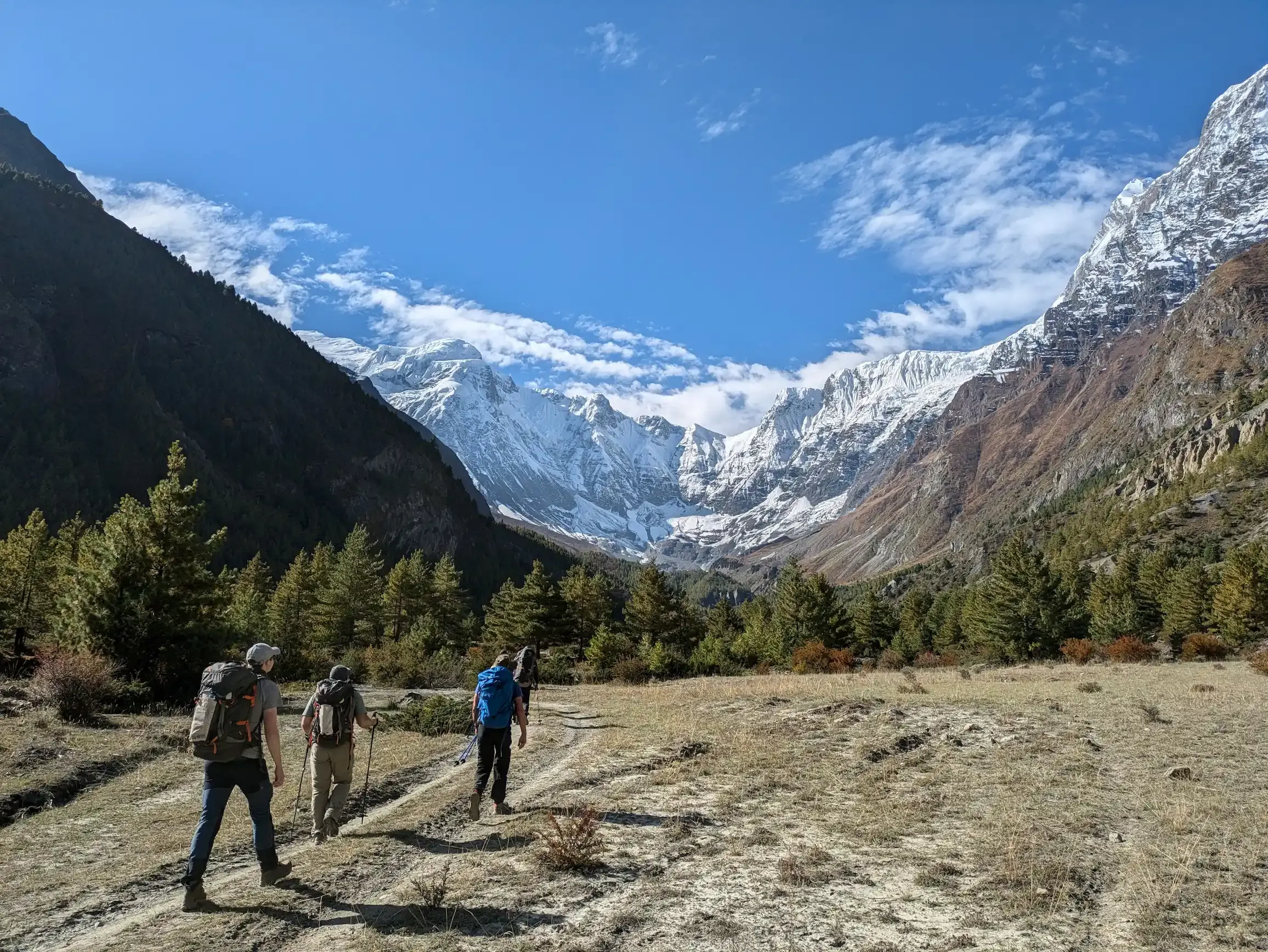 A small group of trekkers crossing a high Himalayan valley toward snow-capped peaks