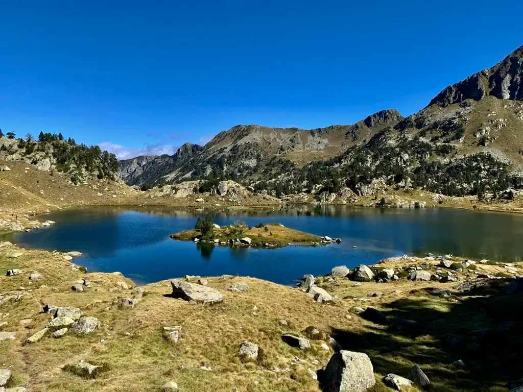 A blue alpine lake ringed by granite peaks and pine forest, high in the Pyrenees